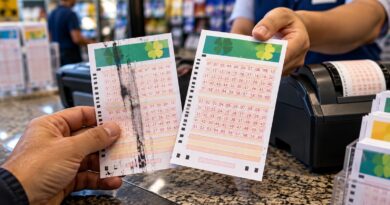 Duas mãos seguram bilhetes de loteria diante de um balcão, um com falha de impressão e outro sem defeitos.